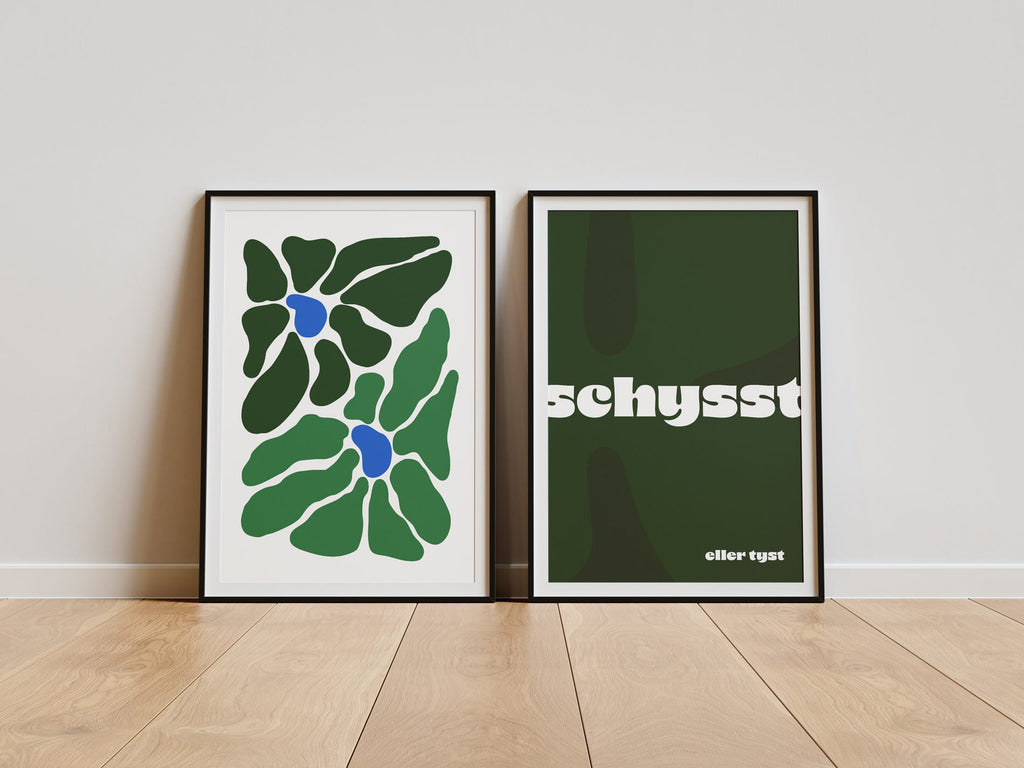 Två inramade posters lutade mot vägg på trägolv – en abstrakt grön poster med blå detaljer och en grön typografisk poster med texten ”schysst eller tyst”.
